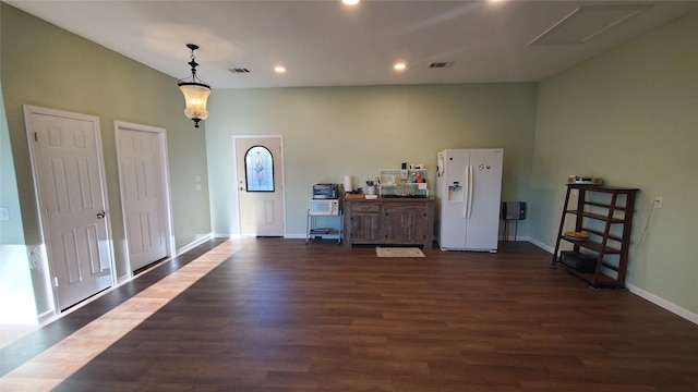 interior space featuring recessed lighting, white refrigerator with ice dispenser, baseboards, hanging light fixtures, and dark wood finished floors