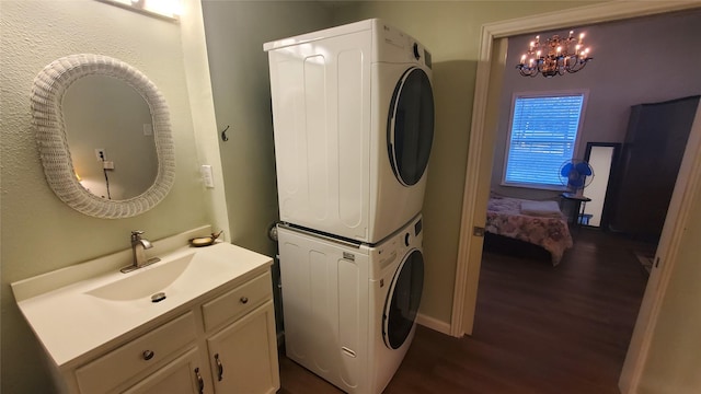 laundry area featuring dark wood-style floors, a notable chandelier, stacked washer / drying machine, cabinet space, and a sink