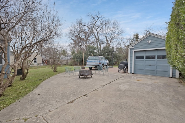 view of patio with a garage, concrete driveway, an outdoor structure, and a fire pit