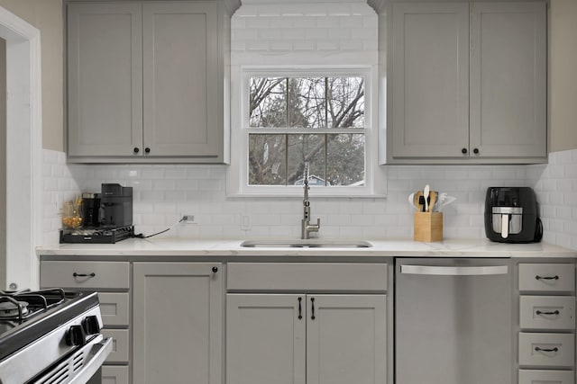 kitchen featuring gray cabinetry, a sink, light countertops, appliances with stainless steel finishes, and tasteful backsplash