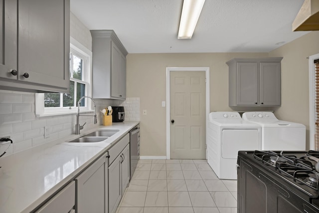 kitchen with gray cabinetry, a sink, washer and dryer, stainless steel dishwasher, and backsplash