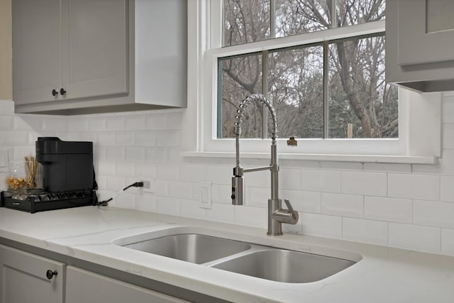 kitchen featuring light stone countertops, tasteful backsplash, a sink, and gray cabinetry