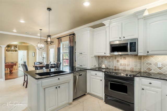 kitchen featuring arched walkways, decorative light fixtures, stainless steel appliances, white cabinets, and a sink