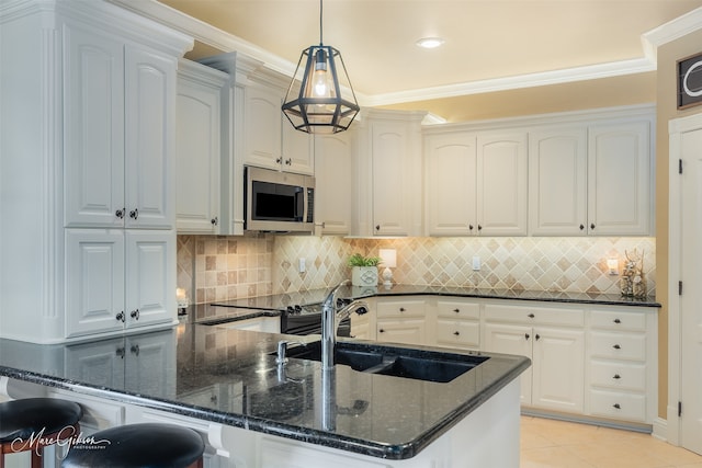 kitchen with dark stone counters, stainless steel microwave, a sink, and white cabinetry