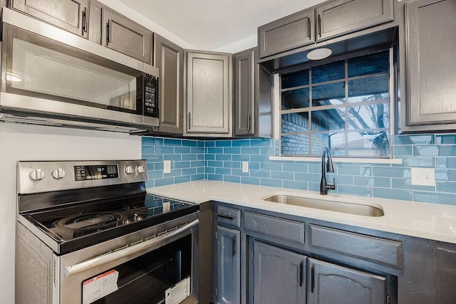 kitchen featuring stainless steel appliances, tasteful backsplash, light countertops, gray cabinetry, and a sink