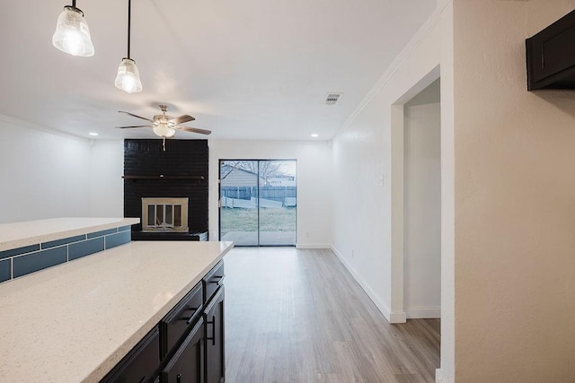 kitchen with baseboards, ceiling fan, ornamental molding, a brick fireplace, and pendant lighting