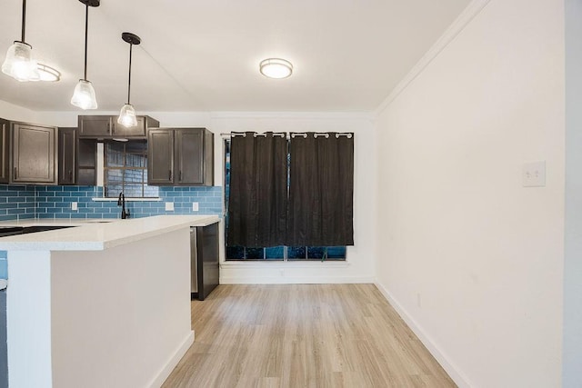 kitchen featuring baseboards, light wood-style floors, light countertops, decorative backsplash, and decorative light fixtures