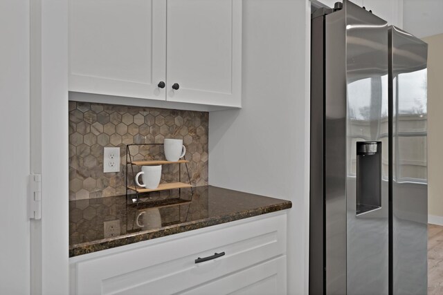 kitchen with dark stone countertops, backsplash, white cabinets, and stainless steel fridge with ice dispenser