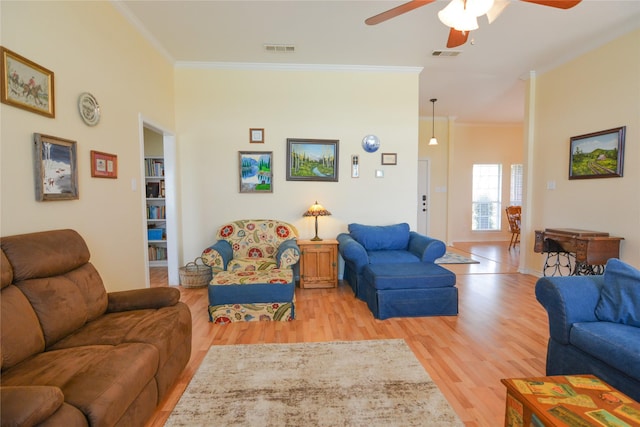 living room with light wood finished floors, ceiling fan, visible vents, and crown molding