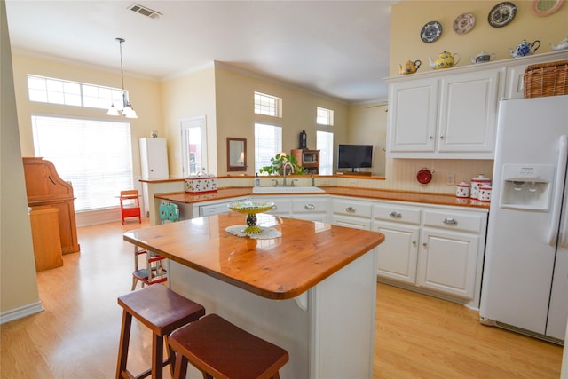 kitchen with white refrigerator with ice dispenser, butcher block counters, visible vents, a sink, and a peninsula