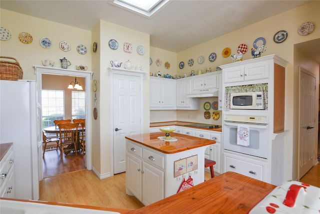 kitchen featuring white appliances, a skylight, under cabinet range hood, white cabinetry, and wooden counters