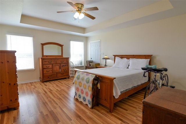 bedroom with a tray ceiling, light wood-style flooring, and a ceiling fan