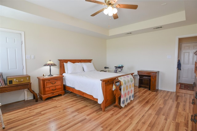 bedroom featuring light wood-type flooring, a raised ceiling, visible vents, and baseboards