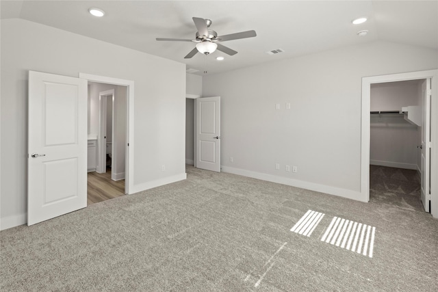 unfurnished bedroom featuring carpet floors, visible vents, vaulted ceiling, and a walk in closet