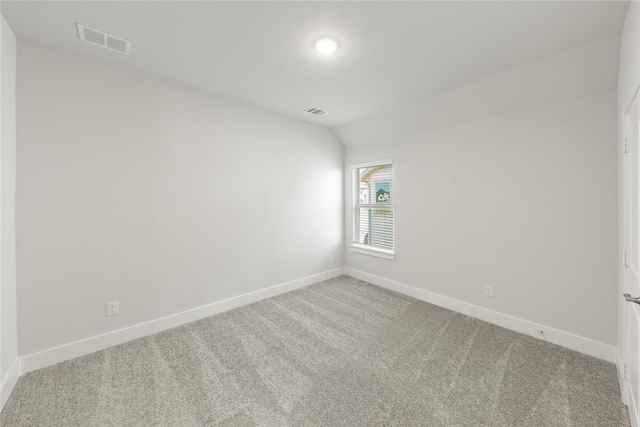 carpeted spare room with lofted ceiling, baseboards, and visible vents