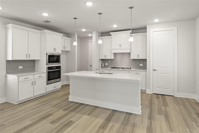 kitchen with stainless steel appliances, light countertops, white cabinets, a sink, and light wood-type flooring