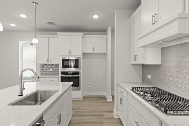 kitchen featuring premium range hood, a sink, white cabinets, appliances with stainless steel finishes, and pendant lighting