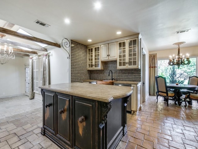 kitchen with light countertops, cream cabinets, an inviting chandelier, glass insert cabinets, and a kitchen island