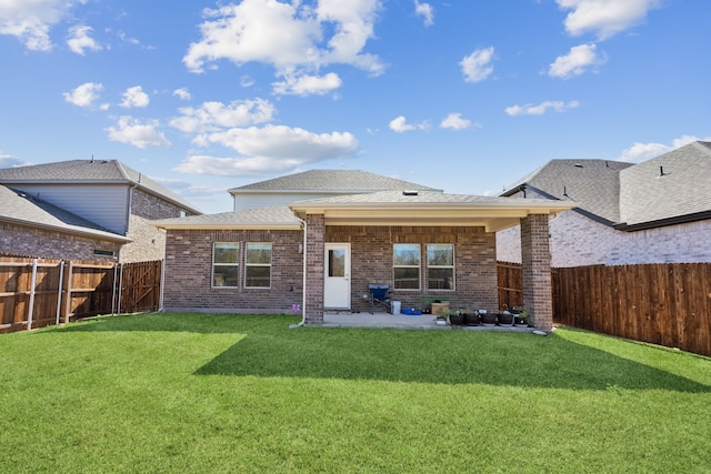 rear view of house featuring brick siding, a patio, roof with shingles, a lawn, and a fenced backyard