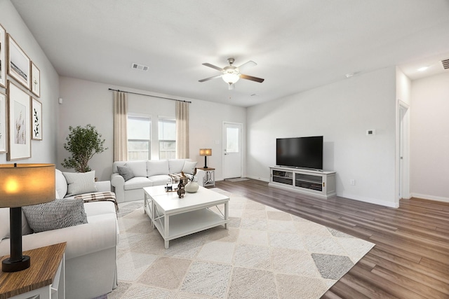 living room with ceiling fan, light wood finished floors, visible vents, and baseboards