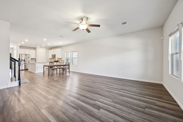 living area with stairs, wood finished floors, visible vents, and baseboards