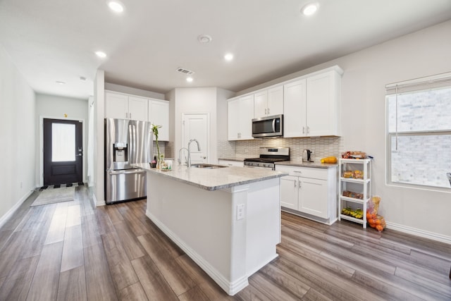 kitchen featuring decorative backsplash, appliances with stainless steel finishes, dark wood-type flooring, a kitchen island with sink, and a sink