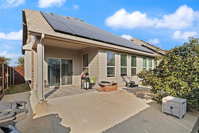 rear view of property featuring roof mounted solar panels, a patio area, and fence