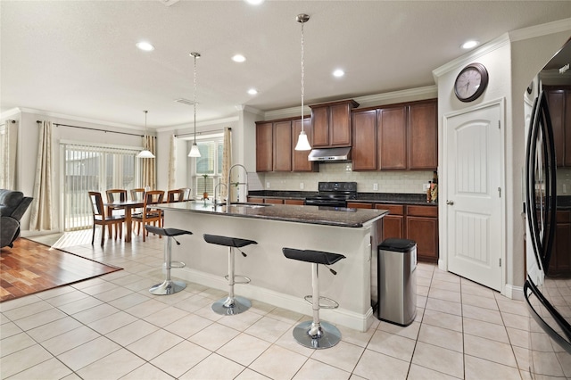 kitchen featuring light tile patterned floors, a kitchen island with sink, black appliances, dark countertops, and pendant lighting