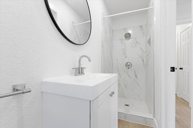 bathroom featuring a textured wall, vanity, a marble finish shower, and wood finished floors