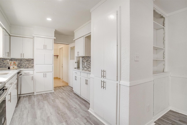 kitchen featuring light wood-type flooring, white cabinetry, light countertops, and decorative backsplash