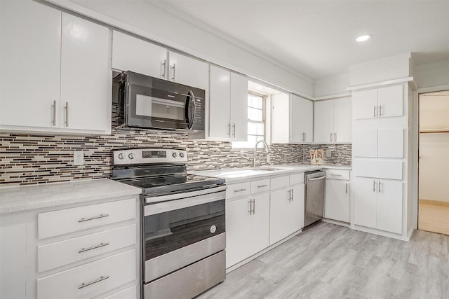 kitchen with stainless steel appliances, a sink, white cabinets, light countertops, and backsplash