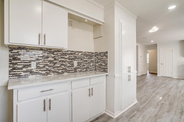 kitchen with decorative backsplash, white cabinets, light stone counters, crown molding, and light wood-style floors