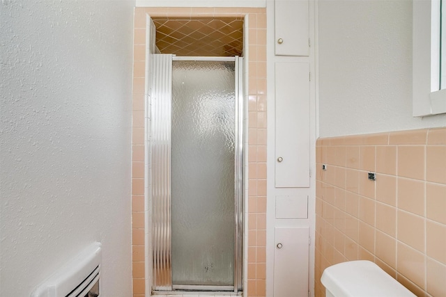 bathroom featuring a stall shower, wainscoting, tile walls, and toilet