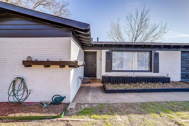 view of exterior entry featuring a patio and brick siding