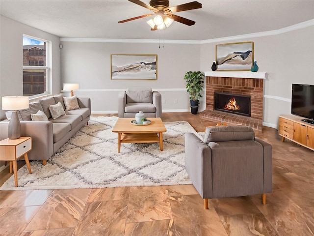 living room featuring a brick fireplace, ceiling fan, baseboards, and crown molding