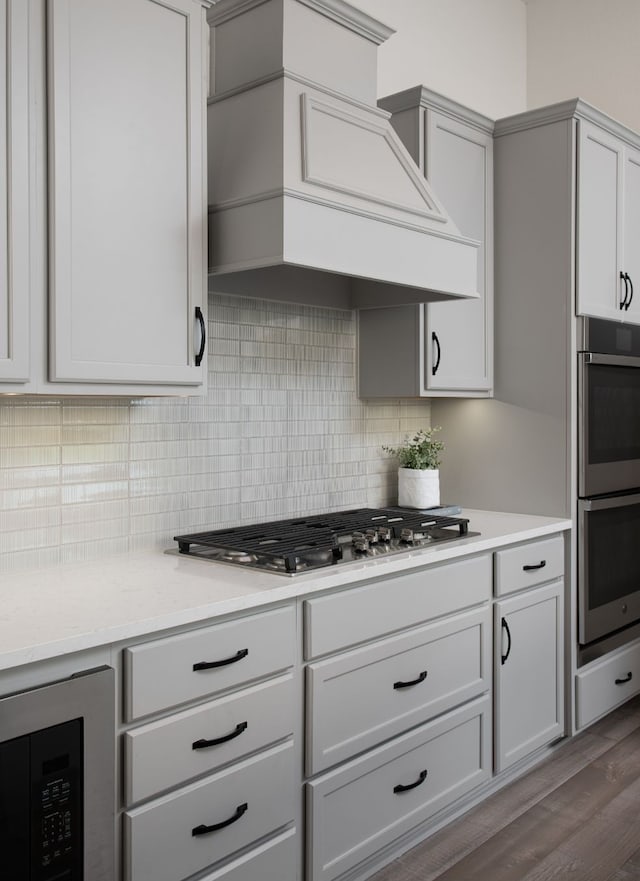 kitchen featuring light stone counters, stainless steel appliances, custom range hood, decorative backsplash, and dark wood-type flooring