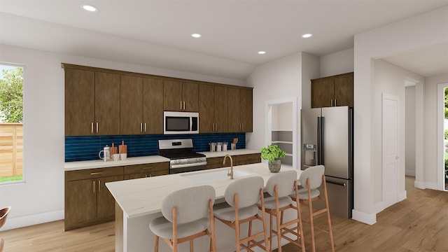 kitchen with stainless steel appliances, a sink, backsplash, and a center island with sink