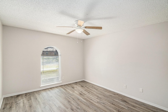 empty room with a ceiling fan, a textured ceiling, baseboards, and wood finished floors