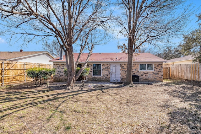 rear view of property with a fenced backyard, brick siding, central AC, and a lawn