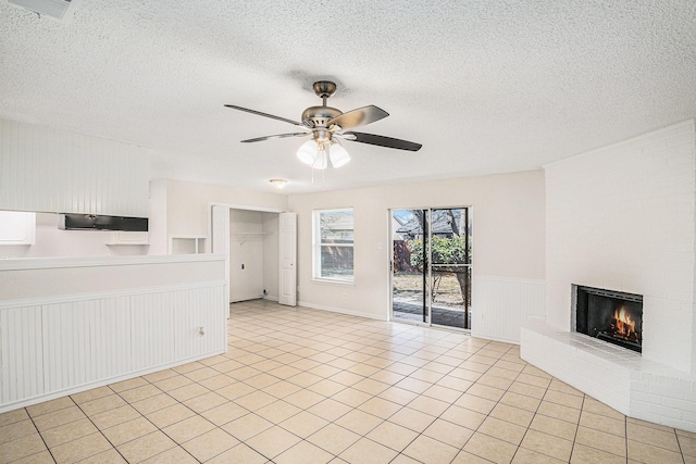 unfurnished living room with a fireplace, visible vents, light tile patterned flooring, ceiling fan, and a textured ceiling