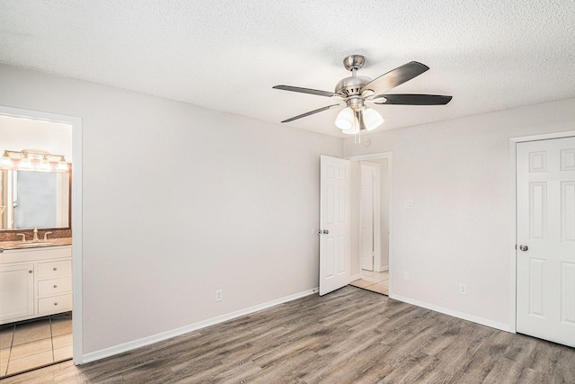 unfurnished bedroom with connected bathroom, a sink, a textured ceiling, wood finished floors, and baseboards