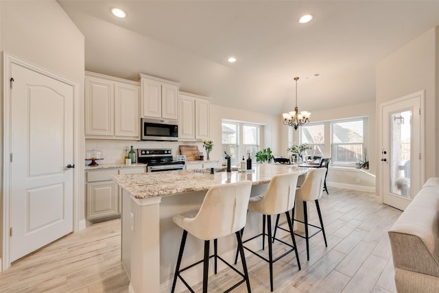 kitchen with a center island with sink, appliances with stainless steel finishes, decorative light fixtures, light stone countertops, and light wood-style floors