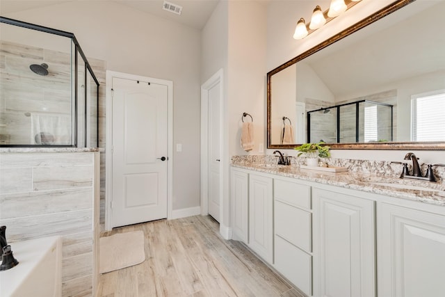 full bathroom with wood finished floors, a sink, visible vents, a shower stall, and double vanity