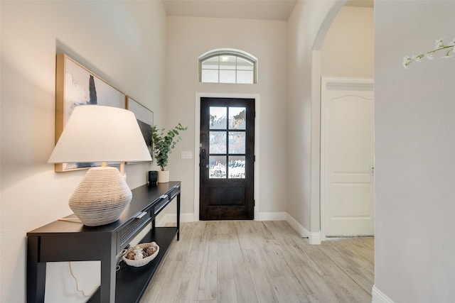 entryway featuring light wood-type flooring, arched walkways, and baseboards