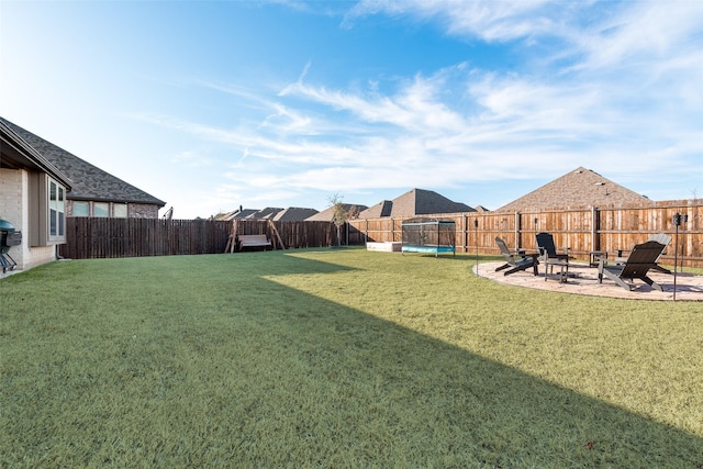 view of yard featuring a trampoline, a patio area, a fenced backyard, and a fire pit