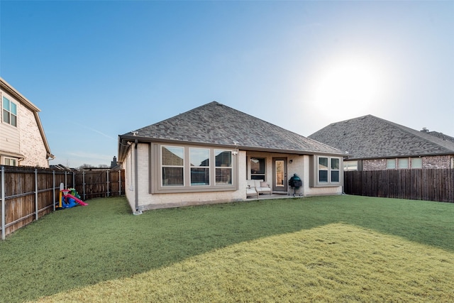 back of property with a shingled roof, a yard, a fenced backyard, and brick siding