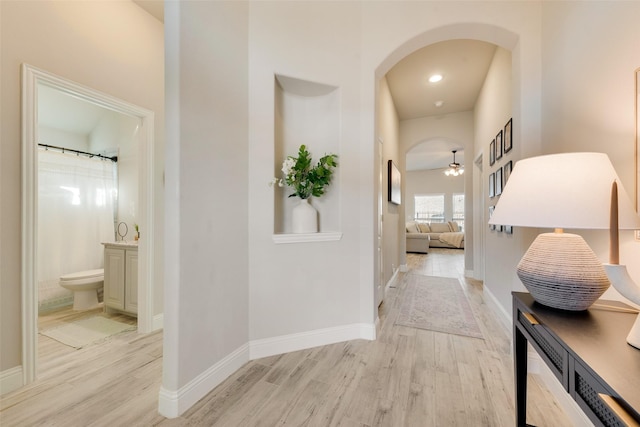 hall with light wood-style floors, arched walkways, and baseboards