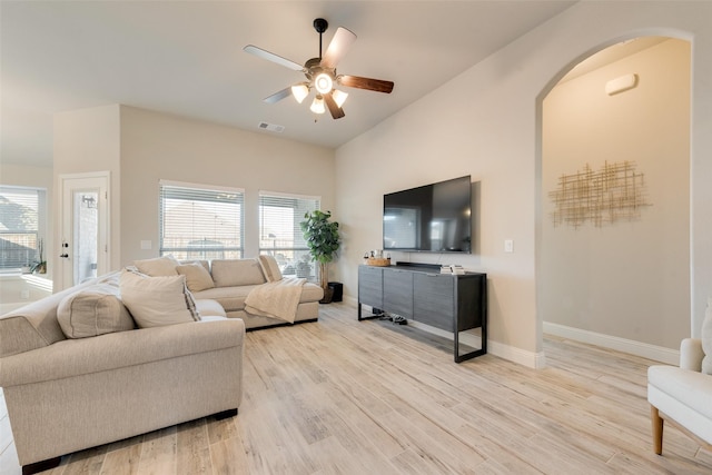 living room featuring baseboards, visible vents, arched walkways, a ceiling fan, and light wood-type flooring