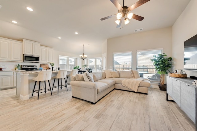 living room with light wood-style floors, recessed lighting, visible vents, and ceiling fan with notable chandelier