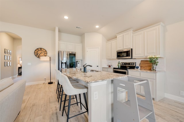 kitchen with arched walkways, stainless steel appliances, a sink, visible vents, and a center island with sink